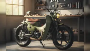 プロのカスタムショップのガレージに置かれた、カーキ色のスーパーカブのカスタムコンプリート車両。ボバースタイルで、ブラウンのソロシートと太いタイヤが特徴的。背景には工具が並び、整備されたプロフェッショナルな雰囲気が漂っている。