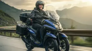 雨上がりの山道を笑顔で快適にツーリングするトリシティ155の日本人ライダー。彼はヘルメットを着用し、ハイスクリーンとサイドケース、トップケースが装着され、カスタムによって快適性が向上している様子。